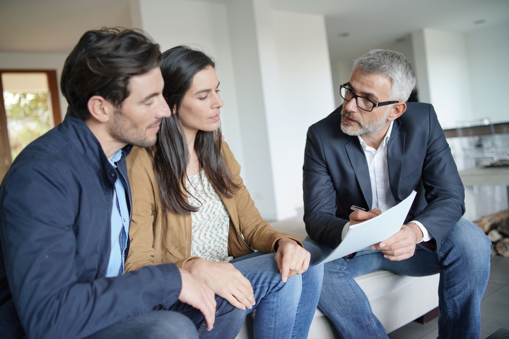Couple,With,Real-estate,Agent,Looking,At,Contract,In,Modern,House